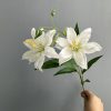 White double petal small lily artificial flower stem closeup, silk faux lily with buds and green leaves