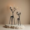 Two black deer candelabra set with lit taper candles on stone display platform