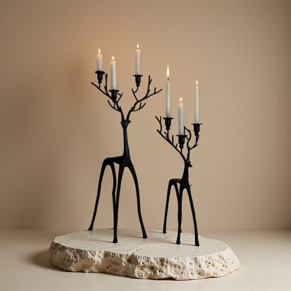 Two black deer candelabra set with lit taper candles on stone display platform